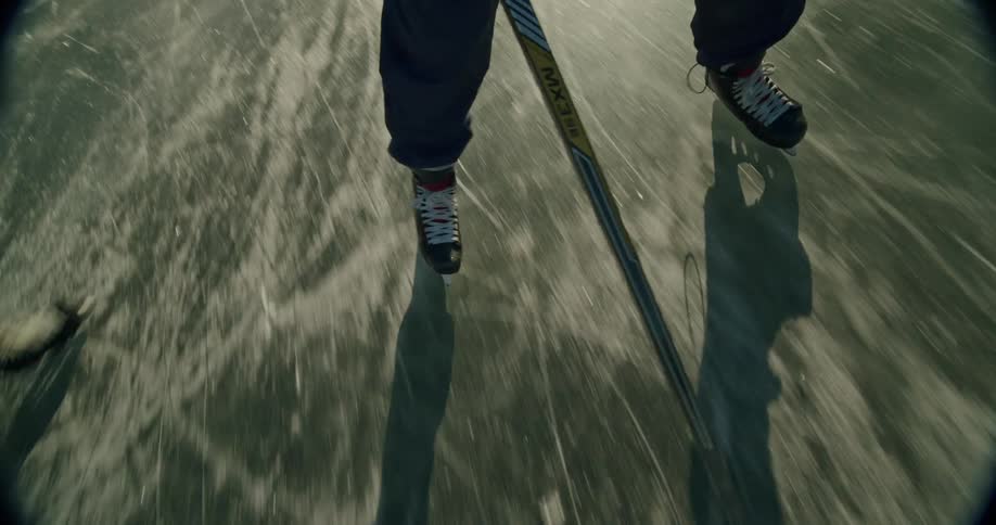 A hockey players feet and stick are shown as they skate and maneuver a puck on the ice