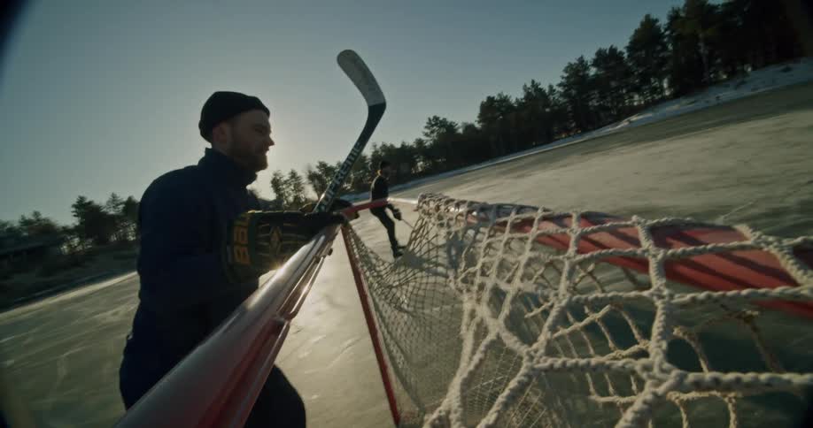 Man skates across a natural outdoor ice rink to place a hockey goal on a sunny day