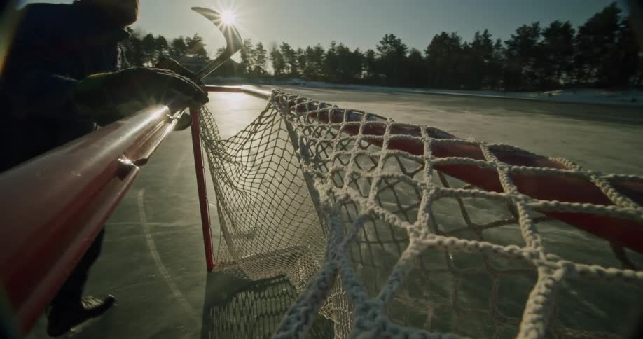 Hockey player moves a goal on the ice outdoors in the sunlight