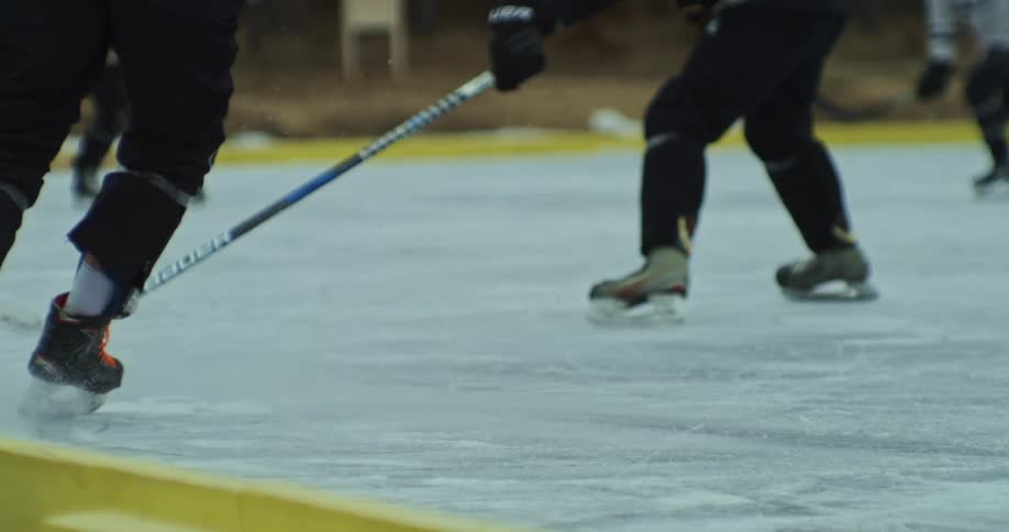 Two people playing hockey on ice and using sticks to hit the puck