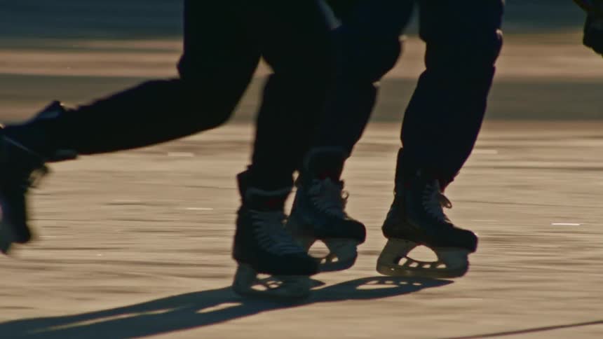 Ice hockey players skates and sticks moving quickly across an outdoor rink
