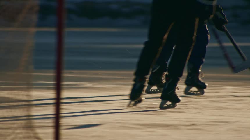 Two people play one on one hockey on an outdoor ice rink