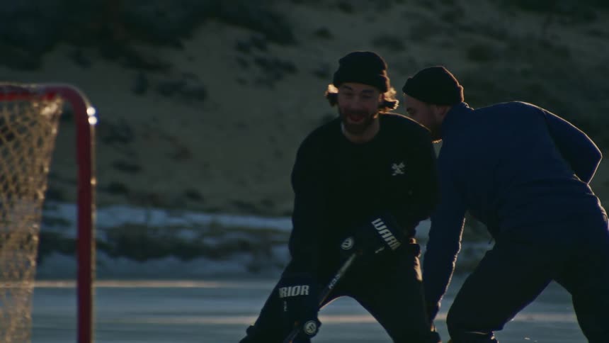 Two male friends are playing ice hockey on a frozen lake