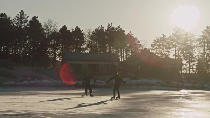 Two men playing a game of hockey on an outdoor ice rink with houses around