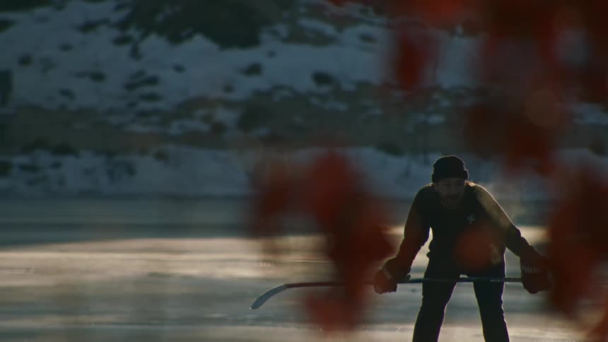Hockey player holds a stick on the ice seen through blurred leaves