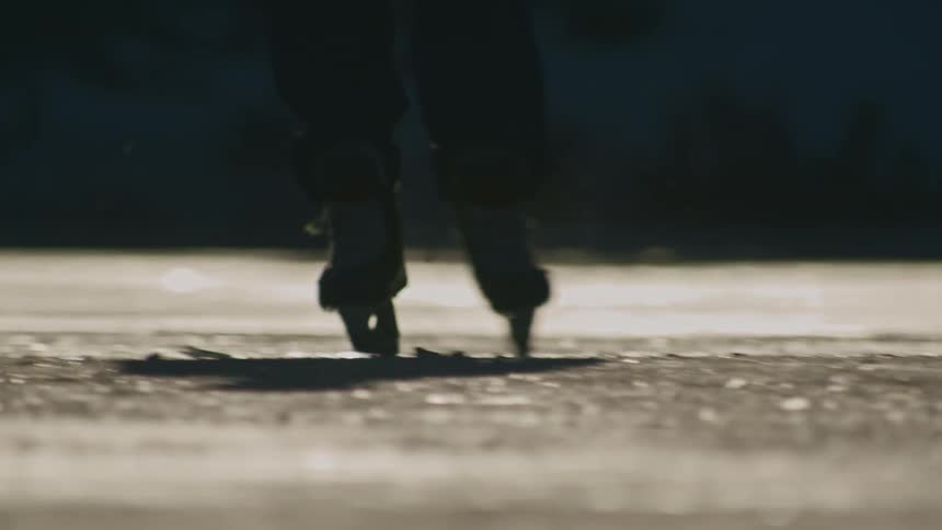 A hockey players skates and stick hitting a puck with ice chips flying