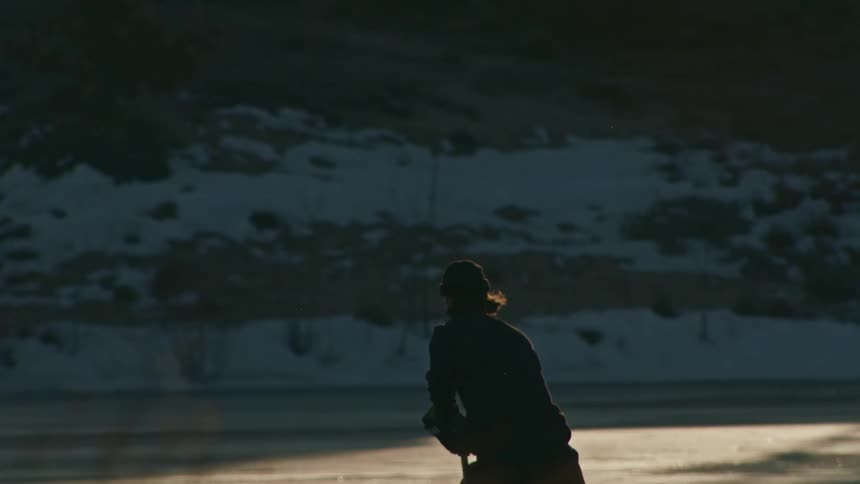 Man skates across an outdoor ice rink with a hockey stick
