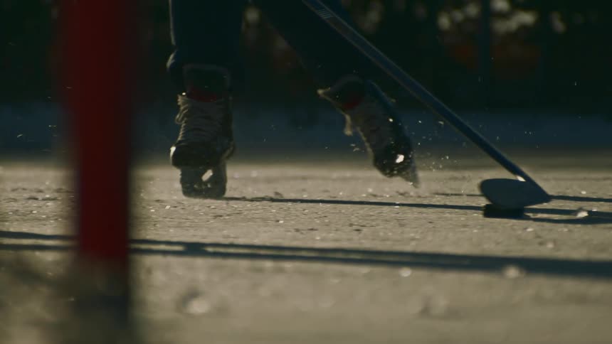 People in ice skates skating over a frozen lake playing hockey in the morning