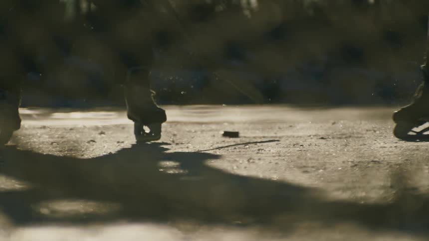 Two people play hockey outdoors on an ice rink