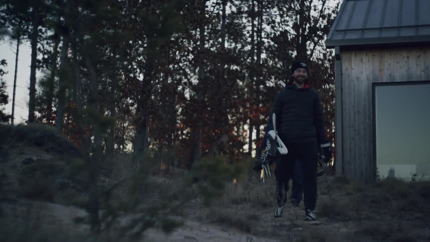 Two men carry hockey equipment past the home