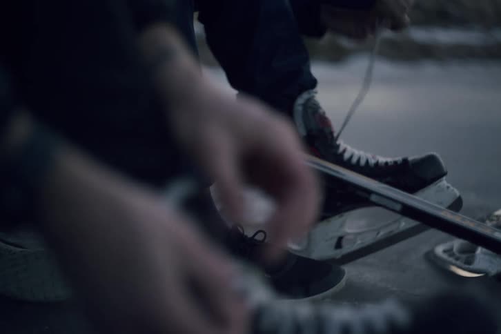 Two men sitting on the ice on a winter day lace up their ice skates before playing hockey