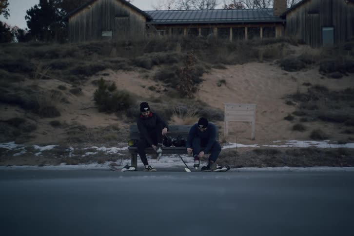 Friends sitting outdoors on bench on frozen pond lacing up hockey skates