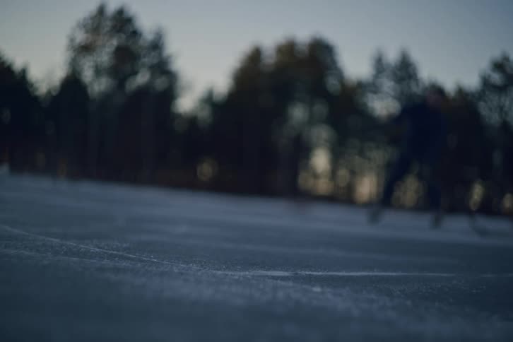 Two men play one on one hockey on an outdoor ice rink near dusk