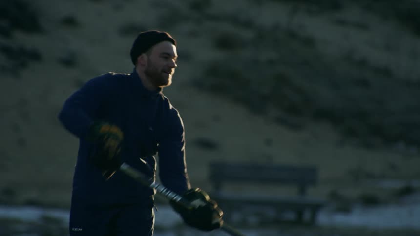 A person wearing a black knit hat and a blue jacket is playing ice hockey in the morning