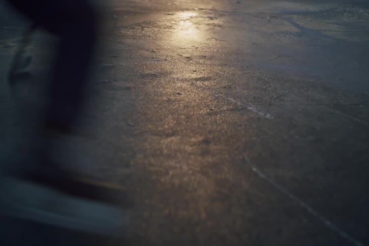 Hockey players skate across an outdoor ice rink near dusk