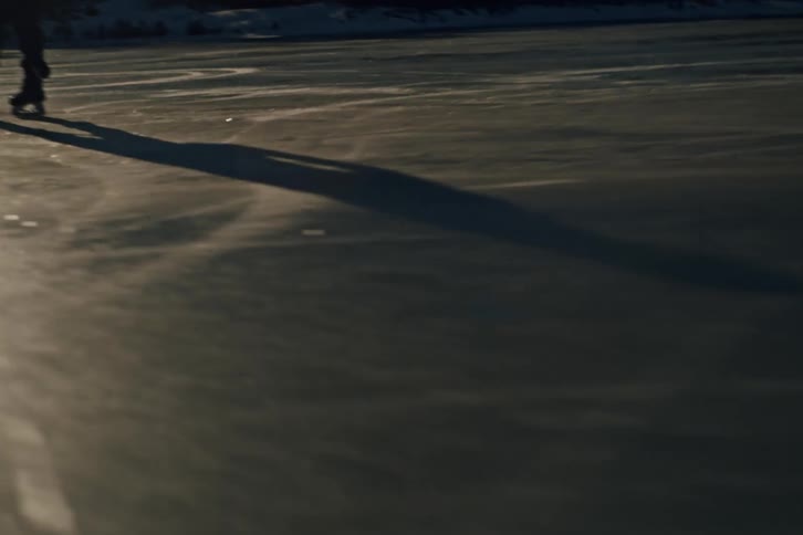 The legs of a person skiing on an icy surface using a hockey stick