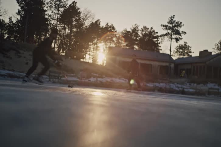 Two people play ice hockey outdoors during sunset