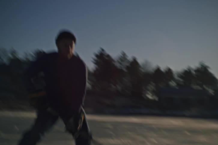 Man manipulates a hockey puck while skating on frozen water in a rural residential area on a winter day