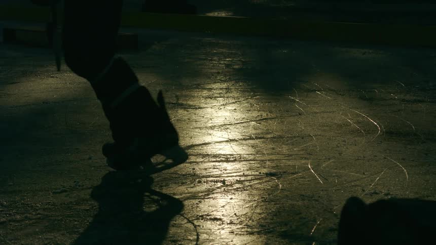 A hockey player silhouetted against the ice reflecting the setting sun skates away from the camera