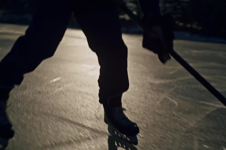 Silhouette of a man playing hockey on a frozen lake at morning