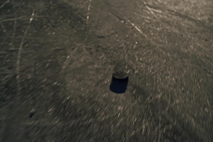 A hockey puck being hit by a stick and spinning as it slides across an ice floor