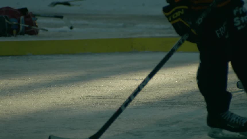 Hockey players skate on an ice rink made on the frozen water at the base of a slope during winter
