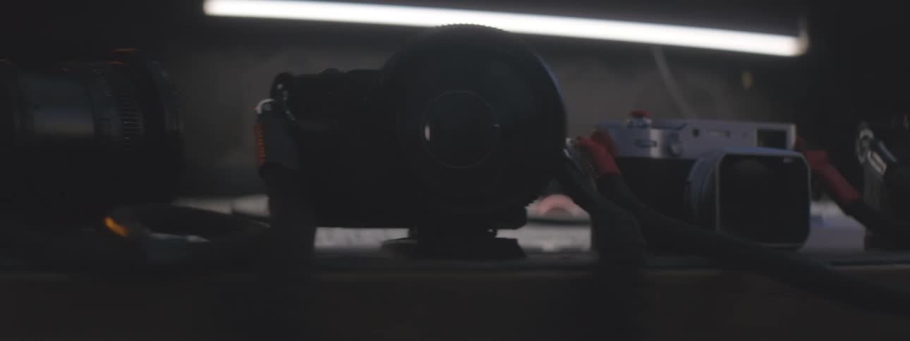 A collection of vintage cameras lined up on a table under a single fluorescent light