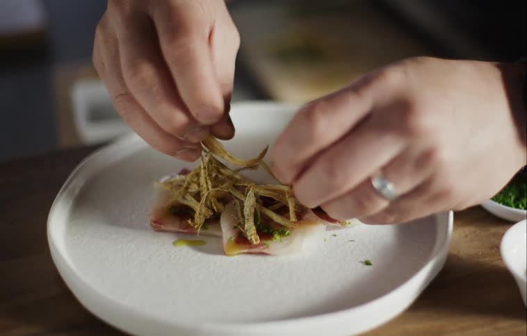 A chef is placing food on a white plate in a restaurant