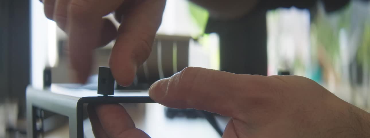 A closeup shot shows a hand adjusting a small black knob on a metal frame