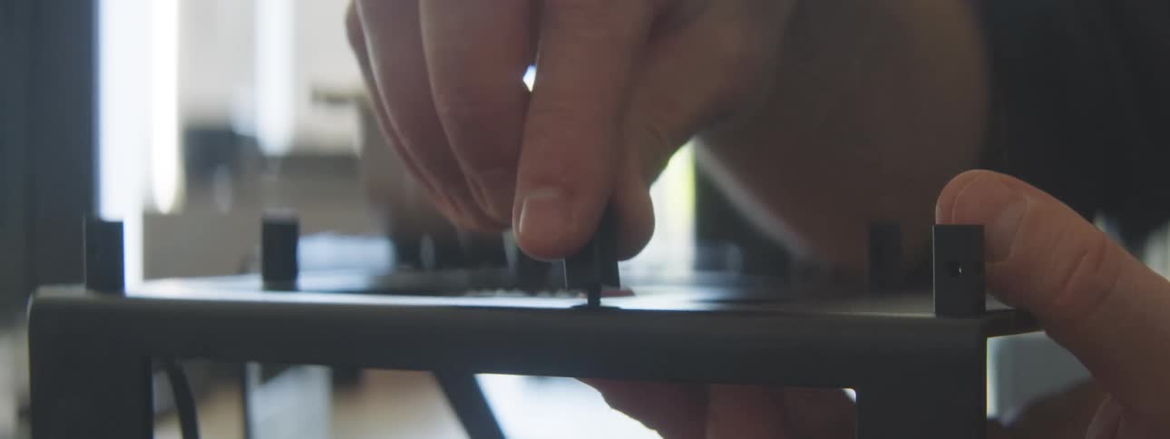 A closeup shot shows a hand adjusting a small black knob on a metal frame