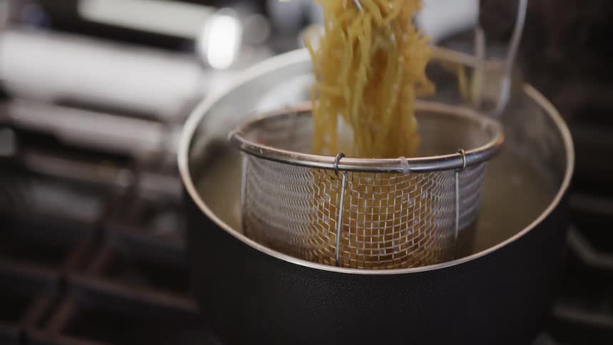 Pasta is cooked in a metal basket inside a pot of boiling water