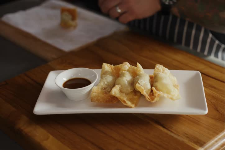 A person using a spoon to put some snacks on a white tray with a brown sauce