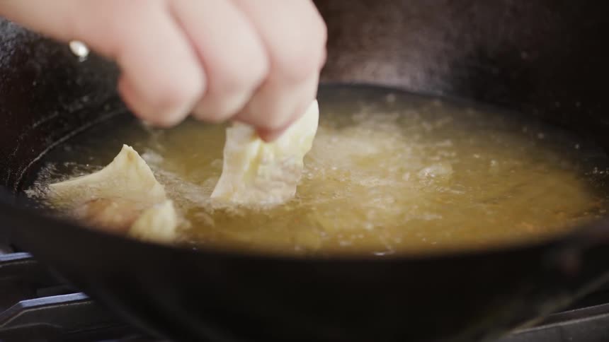 A hand lowers squares of pastry into a pan of hot oil