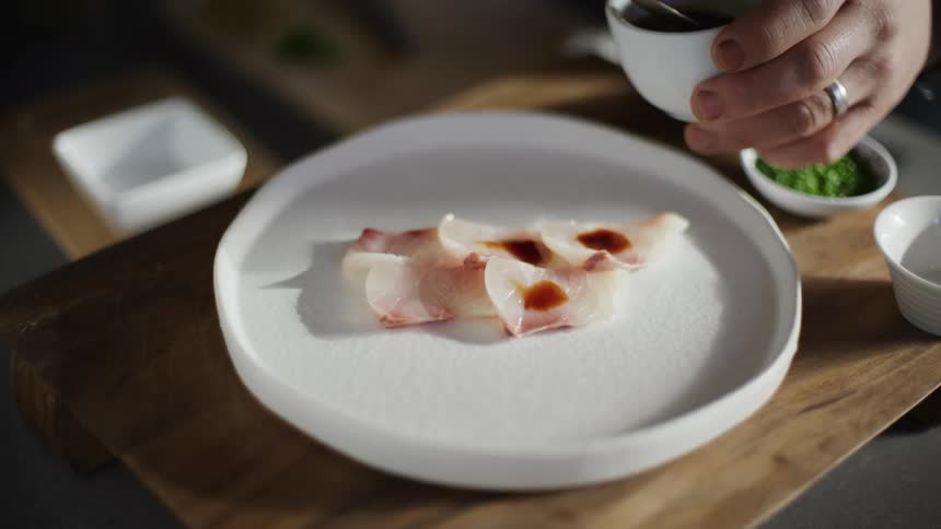 Chef finishes a raw fish dish with a delicate sauce on a white plate