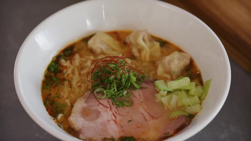Bowl of ramen with seasoned broth sliced beef wontons green onions and chili peppers