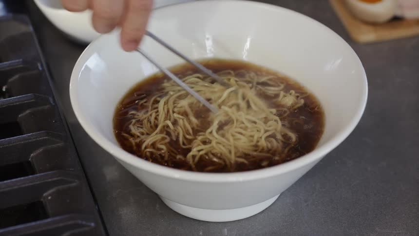 Cooked noodles being poured into a bowl with soy sauce