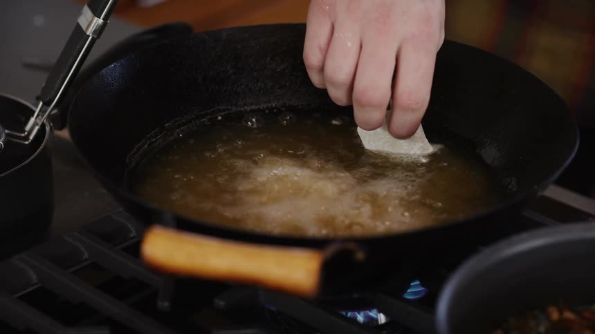 A hand lowers squares of pastry into a pan of hot oil