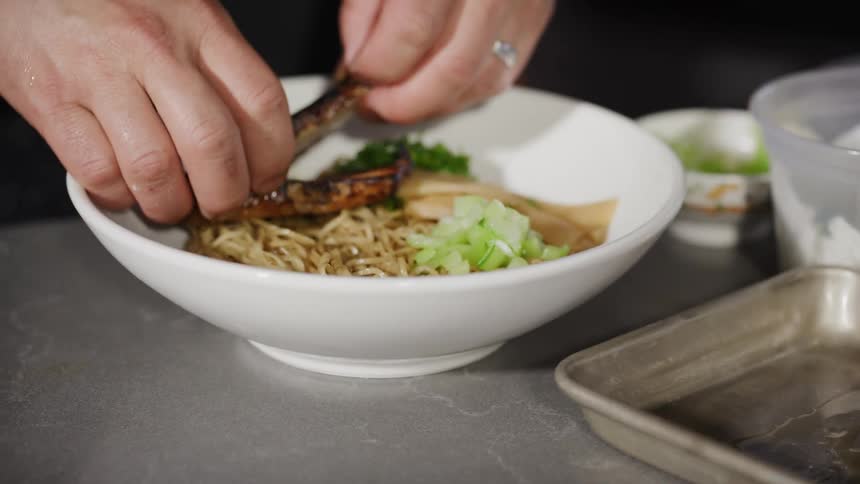 Pair of hands picking up roast pork and placing it on a plate with pasta and salad