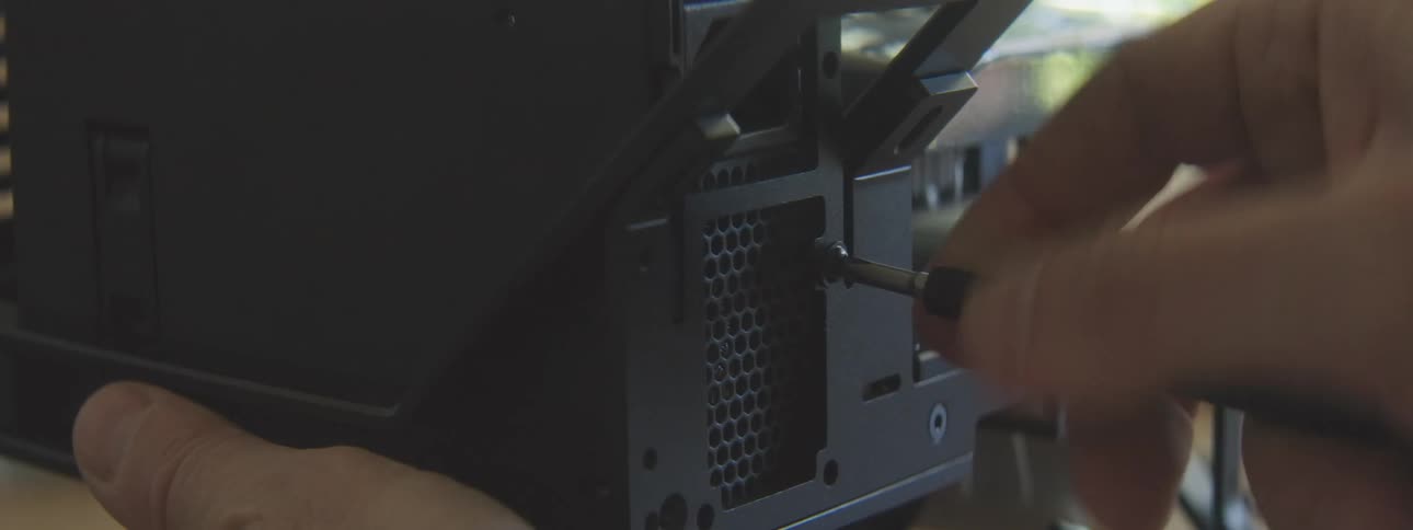 A hand is using a screwdriver to fasten a component onto the back of a black computer case with a honeycomb pattern