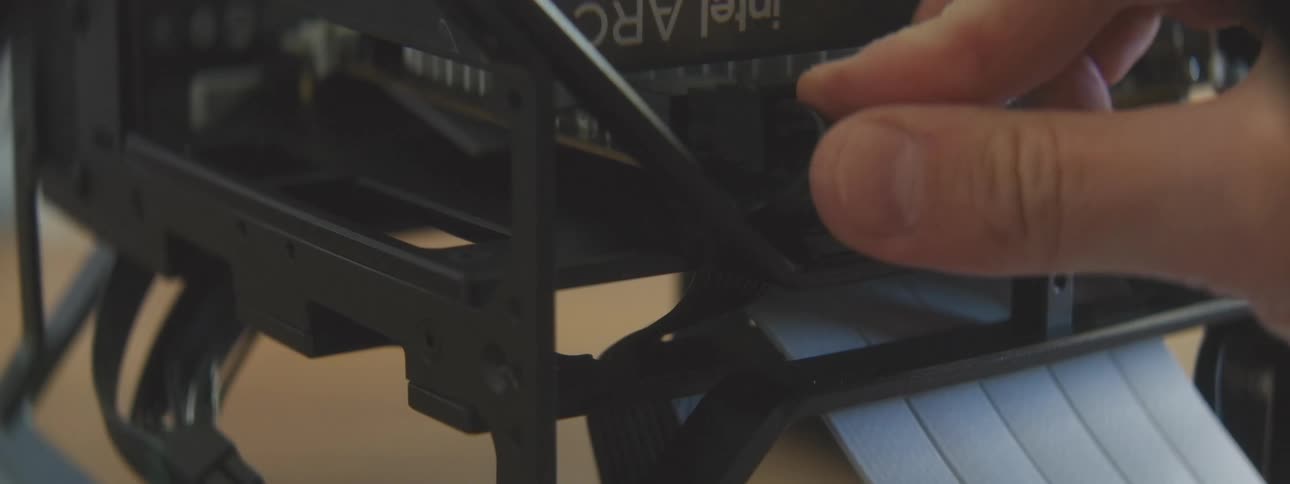 A hand is shown plugging a black cable into a port on a computer component inside a black casing