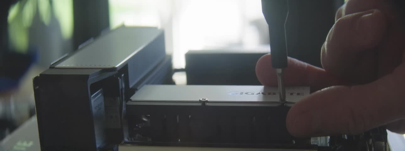 A hand uses a screwdriver to loosen a screw removing a component from a partially assembled computer case