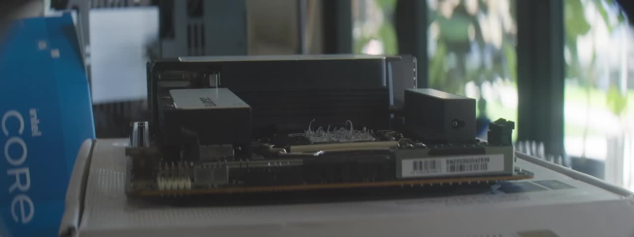 A closeup shot shows a hand adjusting a fan cooler over a computer motherboard