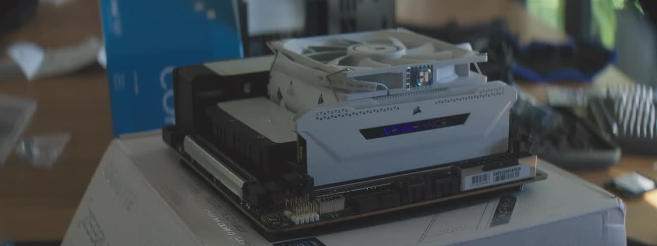Two hands install a ram stick in front of a white fan onto a computer motherboard