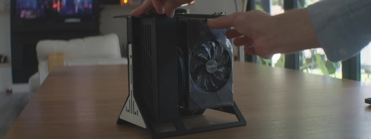 A persons hands peel plastic from the back of a fan on a black computer case with a visible graphics card on a wooden table