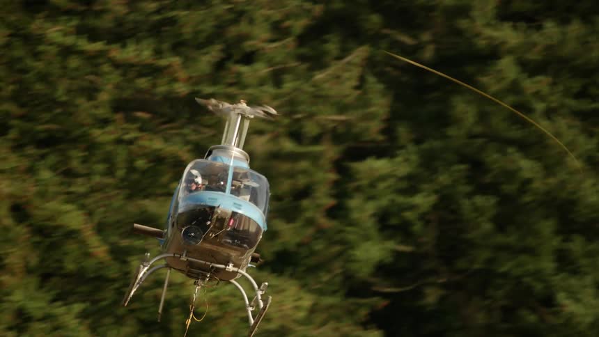 A blue helicopter with cargo hanging by a cable on the underside of the helicopter quickly approaching for a landing