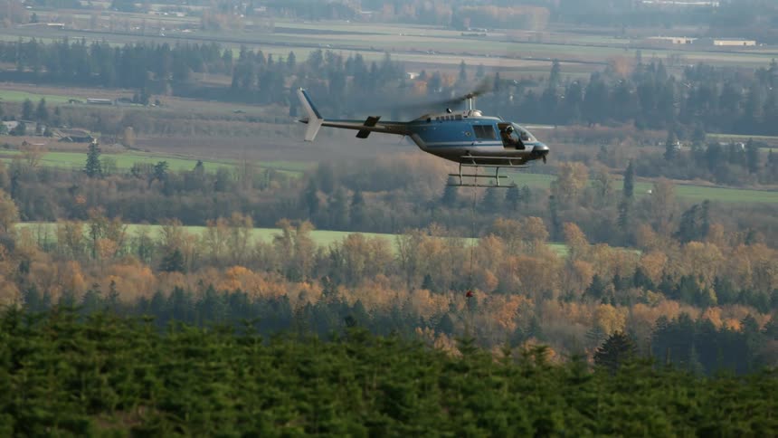Helicopter flying low over a rural area with fields and trees in the background