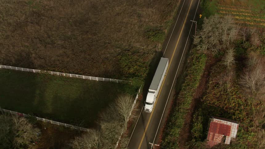 White truck travels along a rural road surrounded by vegetation and small buildings