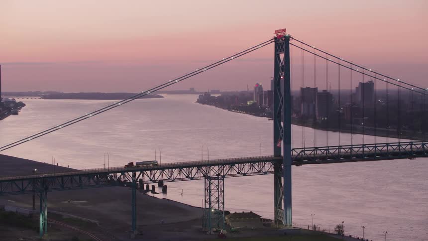 Suspension bridge crossing a river at dusk with a city in the background