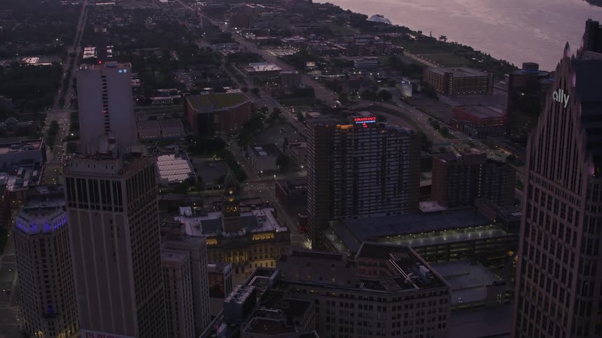Aerial view of a city at dusk with tall illuminated buildings and a river in the background