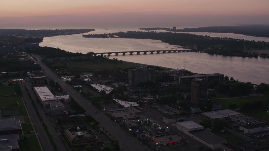 An aerial view shows a city at dusk with a river winding through it and a bridge spanning its waters